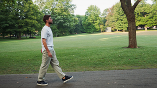 Een man van begin dertig loopt ontspannen over een pad in een groen stadspark in de vroege ochtend