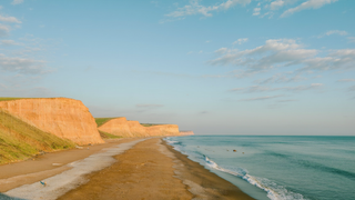 Een brede kust in de Algarve in Portugal in de vroege ochtend, met okerkleurige rotsen, een rustige turquoise zee en een leeg zandstrand