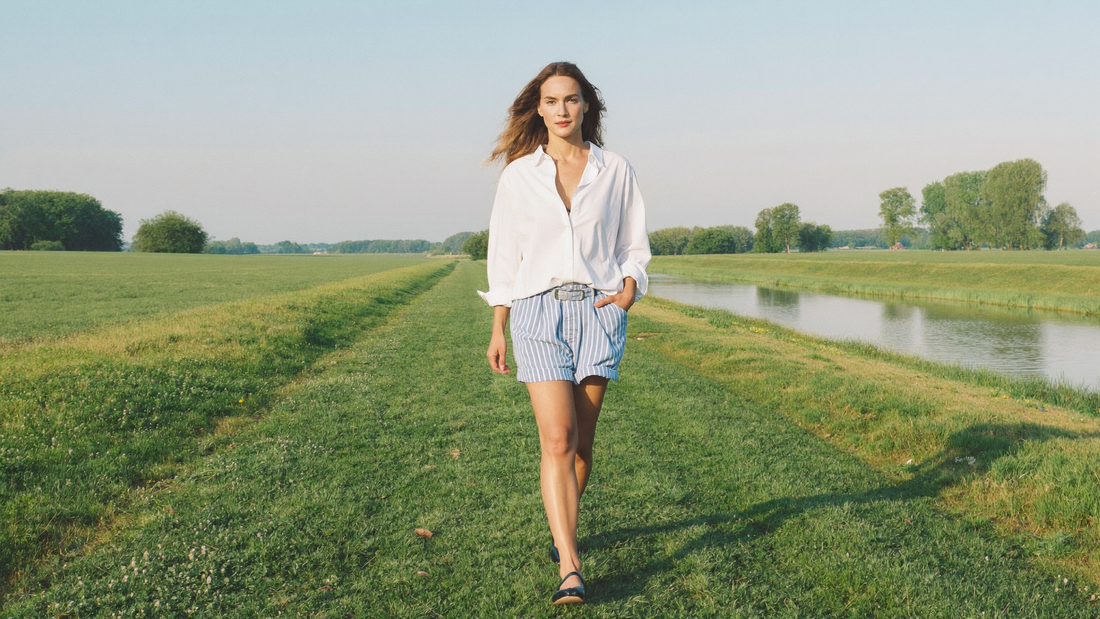 Een vrouw van begin dertig loopt ontspannen over een groene dijk langs weilanden en een rivier