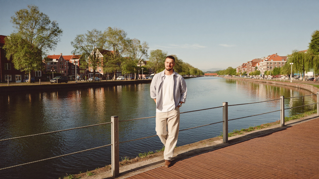 Een man van midden dertig loopt ontspannen langs een rustige gracht in een Nederlandse stad op een heldere ochtend