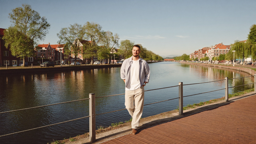 Een man van midden dertig loopt ontspannen langs een rustige gracht in een Nederlandse stad op een heldere ochtend