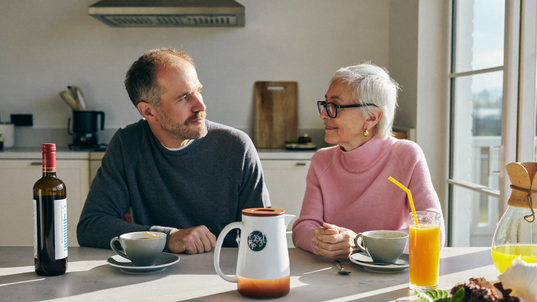 Een stel van in de veertig zit 's ochtends samen aan de keukentafel en praat rustig en aandachtig bij een kop koffie
