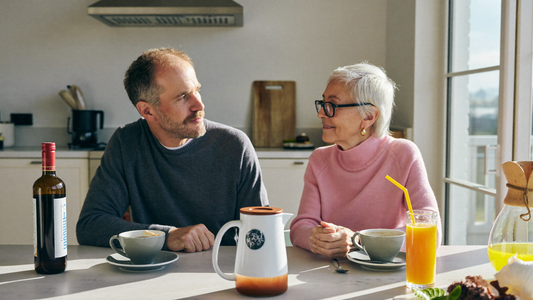 Een stel van in de veertig zit 's ochtends samen aan de keukentafel en praat rustig en aandachtig bij een kop koffie