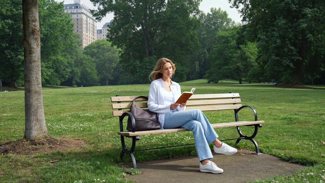 Een vrouw van begin dertig zit ontspannen met een boek op een houten bank in een groen stadspark in de ochtend