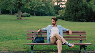 Een man van midden dertig zit ontspannen op een houten bank in een groen stadspark in de ochtend en kijkt rustig voor zich uit
