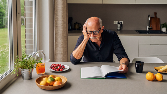 Een man van rond de zestig zit in de ochtend aan een keukentafel bij het raam en kijkt rustig naar een ingelijste foto
