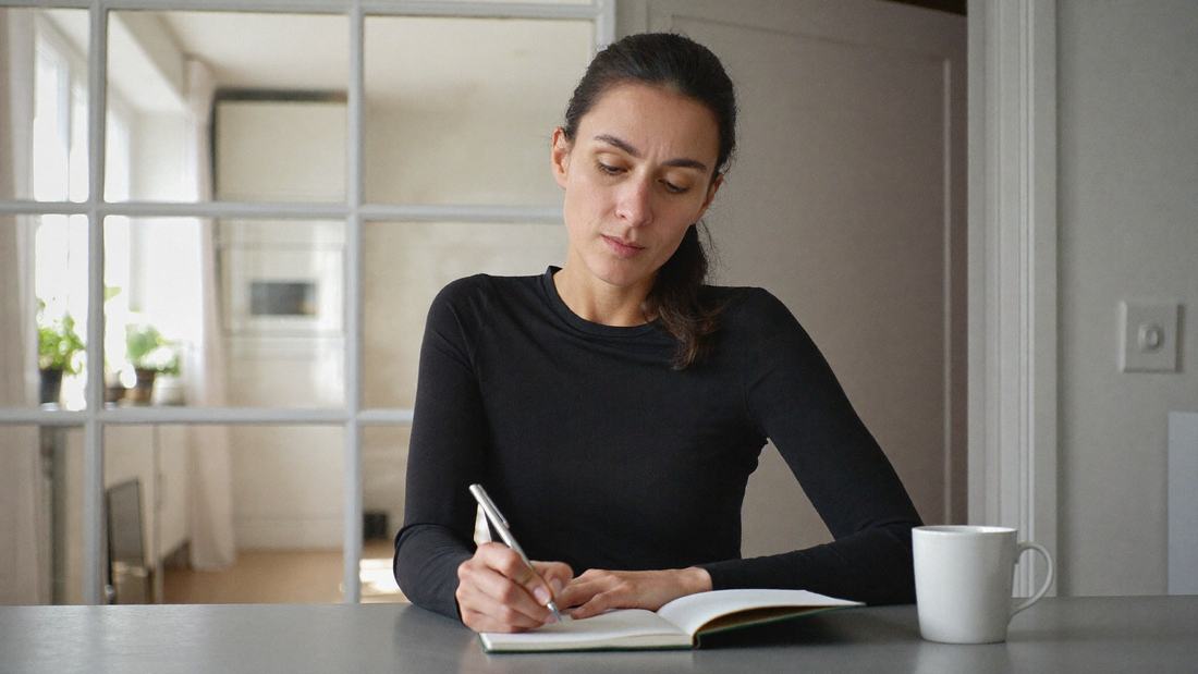 Een vrouw van in de dertig schrijft op een winterochtend in een notitieboek aan de keukentafel