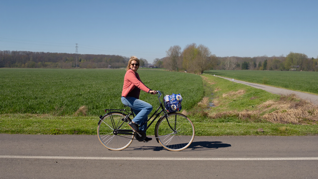 Een vrouw van eind dertig fietst op een heldere lenteochtend over een stille dijkweg langs groene polders