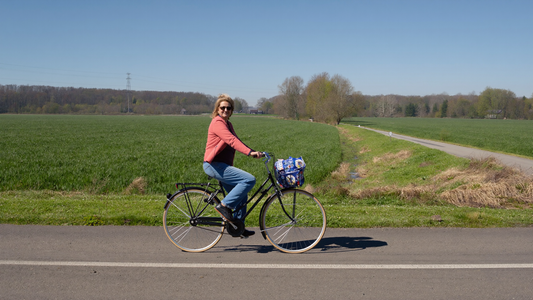 Een vrouw van eind dertig fietst op een heldere lenteochtend over een stille dijkweg langs groene polders