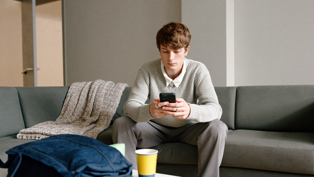 Een jonge man van rond de twintig zit op zijn bank en typt een bericht op zijn telefoon