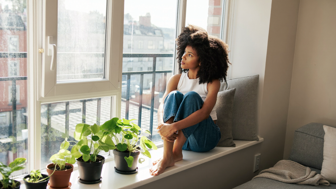 Een vrouw zit rustig in de vensterbank en kijkt naar buiten in het ochtendlicht