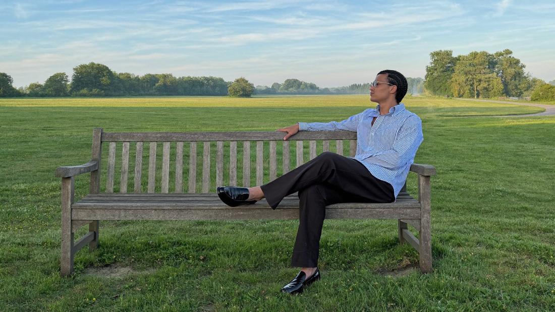 Een man van midden dertig zit ontspannen op een houten bank op een rustige dijk en kijkt in de ochtend uit over wijde groene weilanden