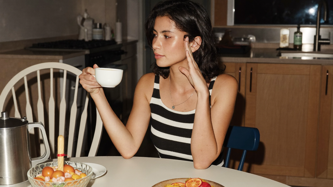 Een vrouw van in de veertig zit 's avonds alleen aan de keukentafel en kijkt peinzend naar haar kop thee