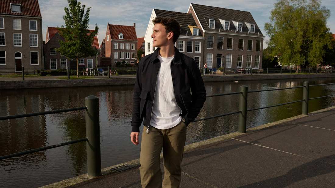 Een man van begin dertig loopt ontspannen langs een rustige gracht in een Nederlandse stad in de vroege avond
