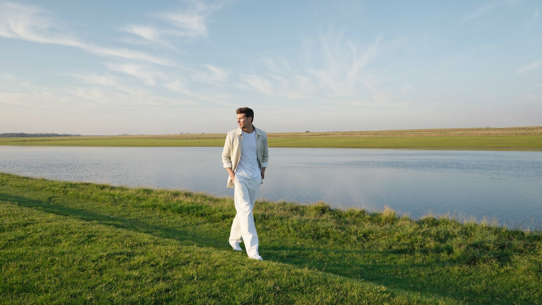 Een man van midden dertig loopt ontspannen over een groene dijk langs een brede rivier in de vroege ochtend