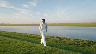 Een man van midden dertig loopt ontspannen over een groene dijk langs een brede rivier in de vroege ochtend