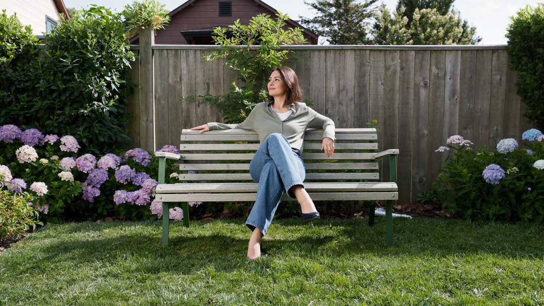 Een vrouw zit ontspannen op een tuinbank in haar eigen achtertuin in de ochtendzon