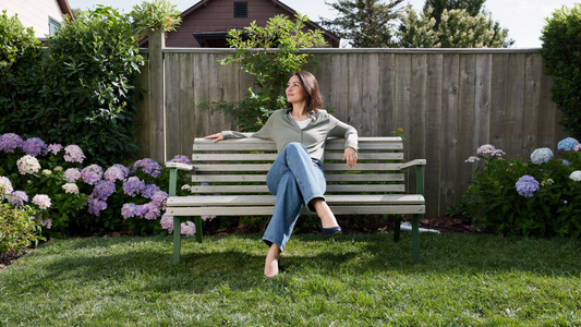 Een vrouw zit ontspannen op een tuinbank in haar eigen achtertuin in de ochtendzon