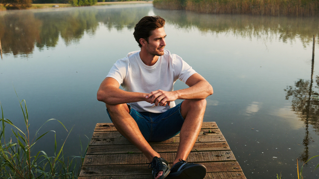 Een man zit in de vroege ochtend op een houten steiger aan een rustig meer en kijkt over het water