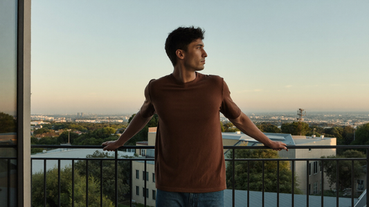 Een jonge man staat in de vroege ochtend op een balkon en kijkt uit over een rustige stad