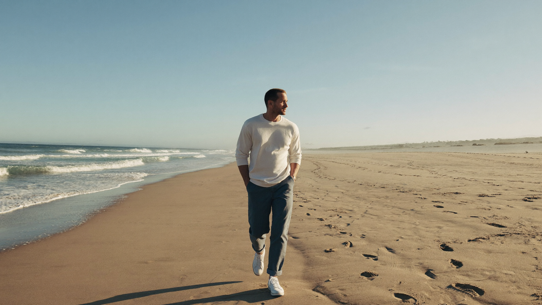 Een man van begin dertig loopt in de ochtend alleen over een breed zandstrand langs de branding
