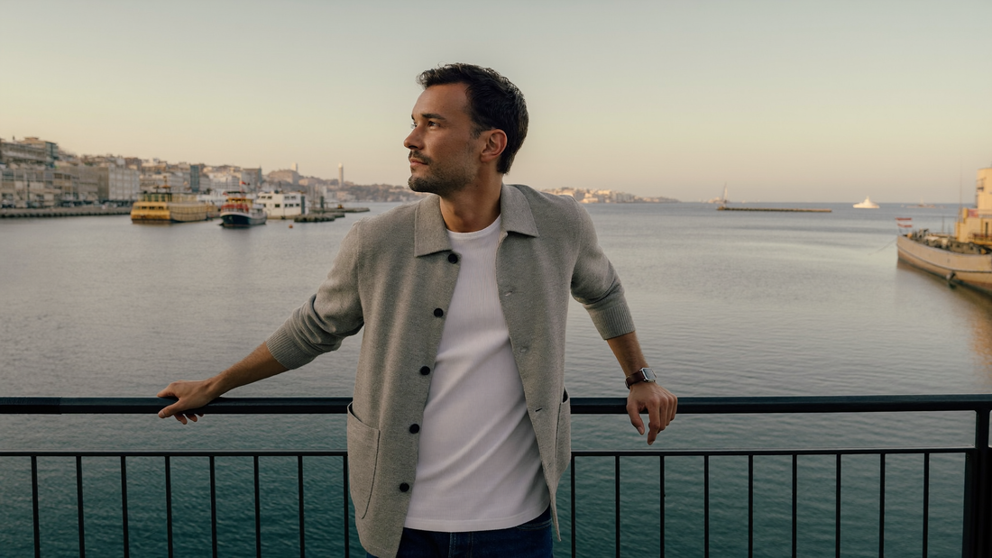 Een man van begin dertig staat in de vroege ochtend aan een reling bij een haven en kijkt over het water