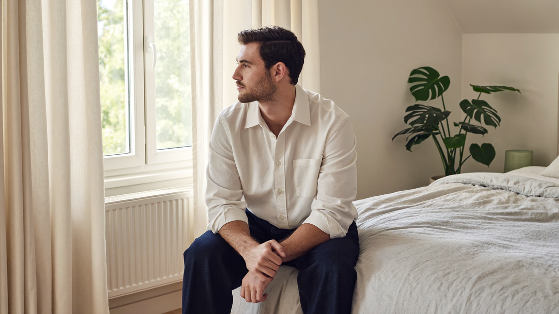 Een man van begin dertig zit op een rustige ochtend op de rand van zijn bed