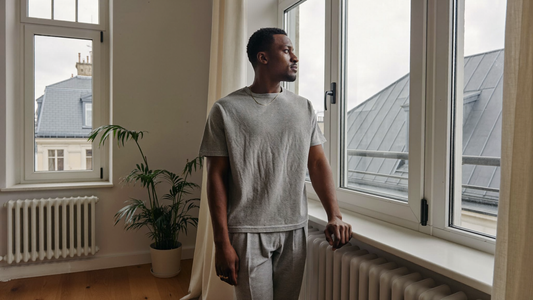 Een man van begin dertig staat op een grijze ochtend voor het raam van zijn appartement
