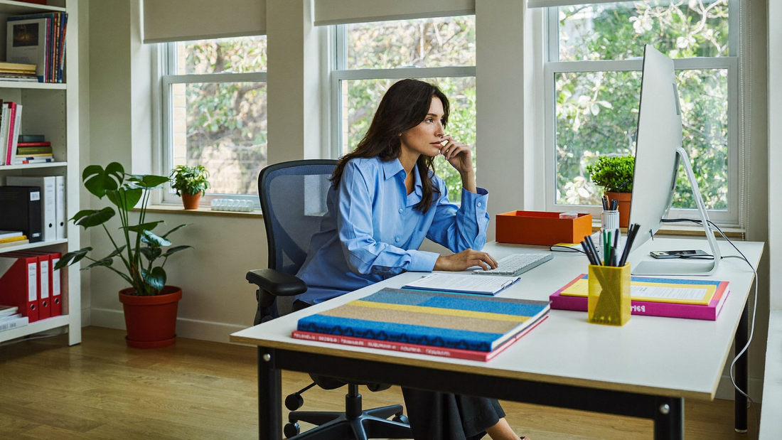 Een vrouw van in de veertig werkt geconcentreerd en rustig aan een bureau in een licht, modern kantoor met planten en grote ramen