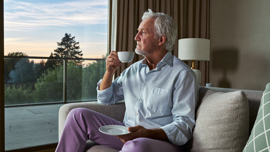 Een man van in de veertig zit 's avonds met een kop thee op de bank, de lamp aan, en kijkt nadenkend naar de zonsondergang