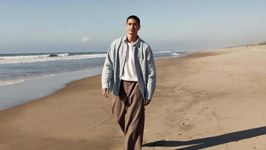 Een man van in de twintig loopt ontspannen over een breed zandstrand in de vroege ochtend