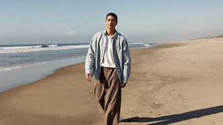 Een man van in de twintig loopt ontspannen over een breed zandstrand in de vroege ochtend