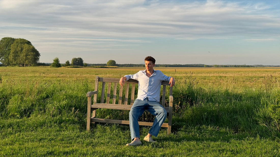 Een man zit ontspannen op een bankje op een dijk en kijkt uit over de polder