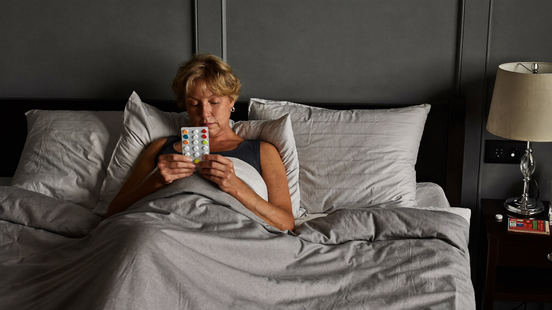 Een vrouw van in de vijftig zit 's nachts rechtop in bed en kijkt naar een strip tabletten op het nachtkastje